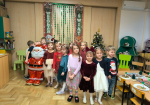 Dzieci stoją przed choinką na tle świątecznych dekoracji