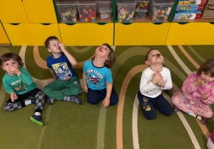 Dzieci siedzą na dywanie z guzikami położonymi na nosie