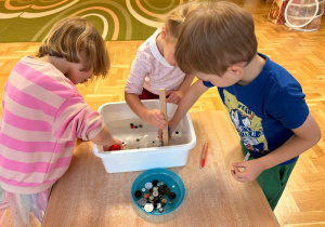 Dzieci wyciągają szczypcami guziki zanurzone w wodzie