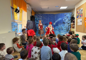 Dzieci siedzą na podłodze i słuchają Świętego Mikołaja