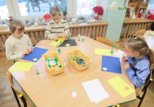 Dzieci przy stoliku wykonują prace plastyczne.