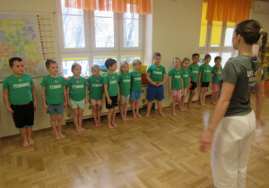 Dzieci stoją w szeregu podczas zajęć gimnastycznych z elementami taekwondo.