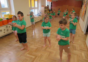 Dzieci stoją w rozsypce w sali podczas zajęć gimnastycznych.