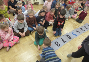 Dzieci układają liczby na podłodze, pozostałe dzieci obserwują.