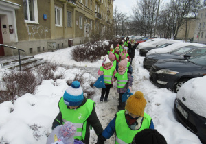 Dzieci idą w parach w odblaskowych kamizelkach.