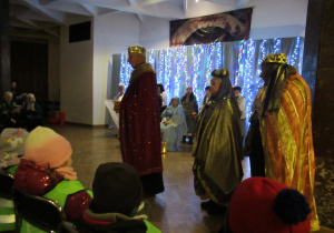 Dzieci oglądają przedstawienie, na scenie seniorzy w strojach.