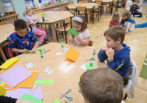 Dzieci siedzą przy stoliku i wycinają.