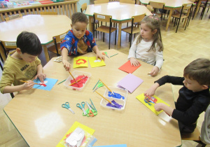 Dzieci siedzą przy stoliku i wykonują laurki.