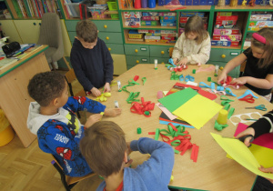 Dzieci siedzą przy stoliku i wykonują kwiaty z papieru.