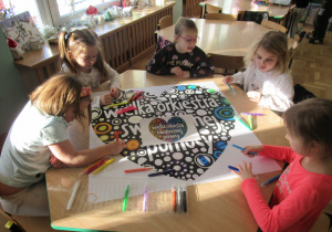 Dziewczynki siedzą przy stoliku i kolorują plakat.