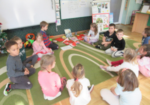 Dzieci siedzą na dywanie podczas zajęć.