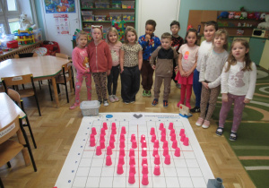 Dzieci podczas zajęć z elementami kodowania, przed nimi mata do kodowania, na macie ułożone serce z różowych kubeczków.