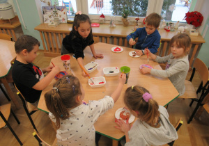 Dzieci przy stoliku malują serca z masy solnej.