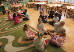 Dzieci siedzą w małych kółeczkach i podają sobie balony.