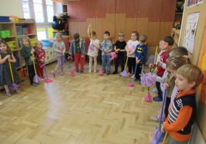 Dzieci tańczą z "miotełkami" podczas zajęć z rytmiki.