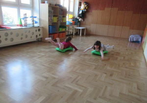 Dziewczynki jadą na jeździkach gimnastycznych.