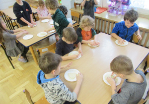 Dzieci siedzą przy stolikach i lepią z masy solnej.