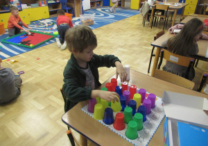 Chłopiec przy stoliku układa kolorowe kubeczki na mini macie do kodowania.