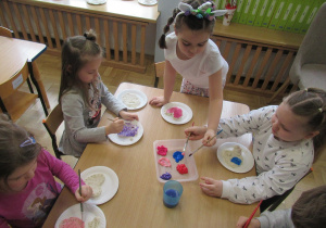 Dziewczynki przy stoliku malują farbami serca z masy solnej.