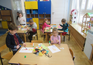 Dzieci wykonują prace plastyczne przy stolikach.