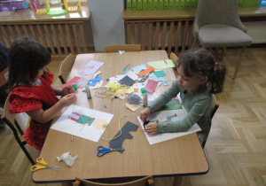 Dziewczynki przy stole wykonują prace plastyczne.