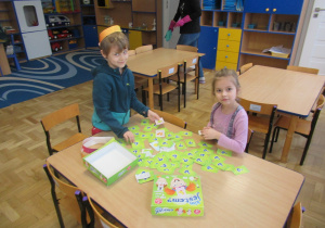 Chłopiec i dziewczynka przy stoliku grają w grę "Kim jestem?".