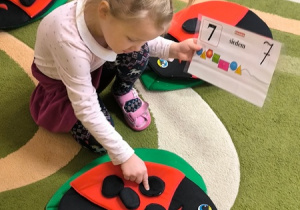Dziewczynka dopasowuje planszę z cyfrą do materiałowej biedronki