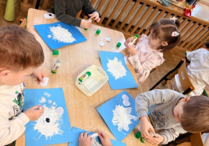 Dzieci przyklejają na kartkę papierowe śnieżynki