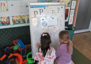 Dziewczynki piszą litery p na tablicy.