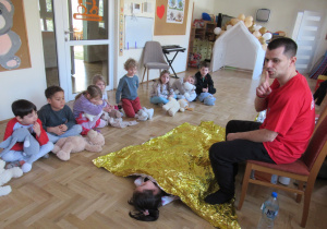 Dziewczynka leży na podłodze przykryta kocem termicznym podczas warsztatów z pierwszej pomocy.