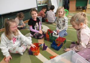 Dzieci siedzą na dywanie i bawią się klockami.