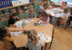 Dzieci siedzą przy stolikach i malują farbami.