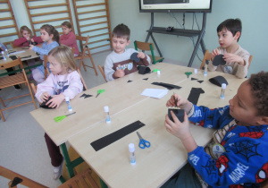 Dzieci przy stolikach wykonują koty z papieru.