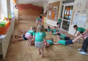 Część dzieci leży na brzuchu, kilkoro dzieci trzyma je za nogi.