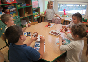 Dzieci siedzą przy stoliku i malują farbami.