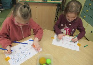 Dziewczynki siedzą przy stoliku i wykonują ćwiczenie na koncentrację uwagi.