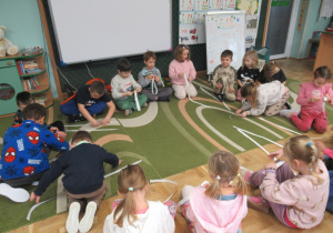 Dzieci siedzą w kole, każde z dzieci trzyma w ręku miarkę.