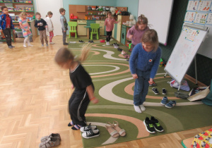 Dzieci skaczą w sali obok ścieżki ułożonej z butów.