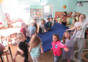 Dzieci trzymają za krawędzie niebieski materiał.