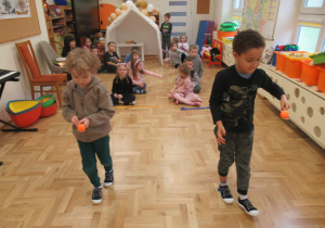 Chłopcy przenoszą piłeczki na drewnianych łyżkach, pozostałe dzieci siedzą w dwóch rzędach.