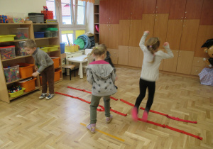 Dzieci przeskakują przez ułożone na podłodze szarfy.