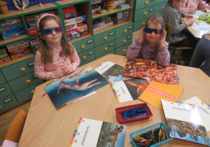 Dziewczynki oglądają obrazki dinozaurów w okularach 3D.