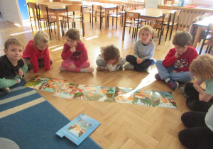 Dzieci siedzą na podłodze, przed nimi leżą obrazki.