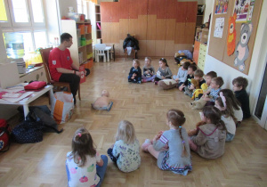 Dzieci siedzą w półkolu podczas warsztatów "Akademia Małego Ratownika".