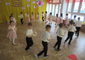 Dzieci tańczą tworząc koło, w rękach trzymają świecące serca.