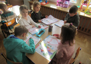 Dzieci siedzą przy stoliku i pracują w książkach.