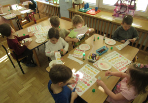 Dzieci siedzą przy stolikach i wycinają.