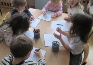 Dzieci siedzą przy stolik i wykonują karty pracy.