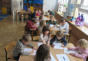 Dzieci siedzą przy stolikach i wykonują karty pracy.