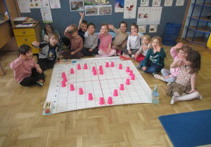 Dzieci siedzą wokół maty do kodowania, na macie serce ułożone z kubeczków.